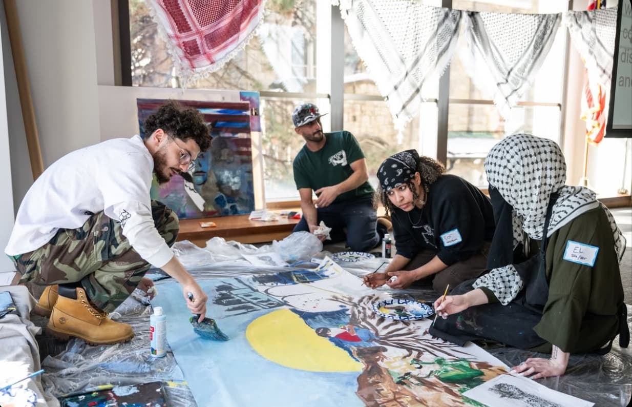 Young artists kneeling on the floor together painting a large figurative canvas mural