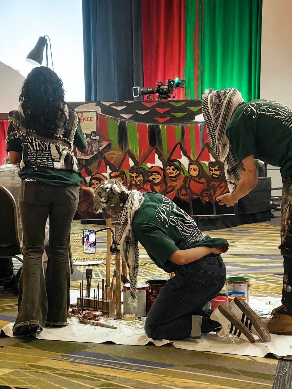 Artists painting a large figurative mural on a stage against a red, green, and black backdrop