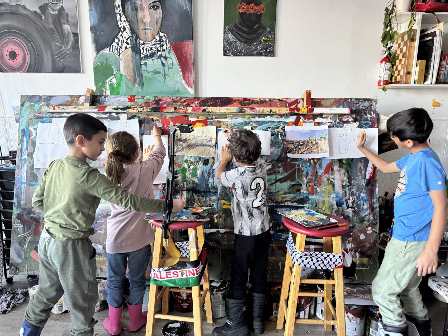 Children painting a large collaborative canvas in the studio, Palestinian portrait paintings on the walls behind them