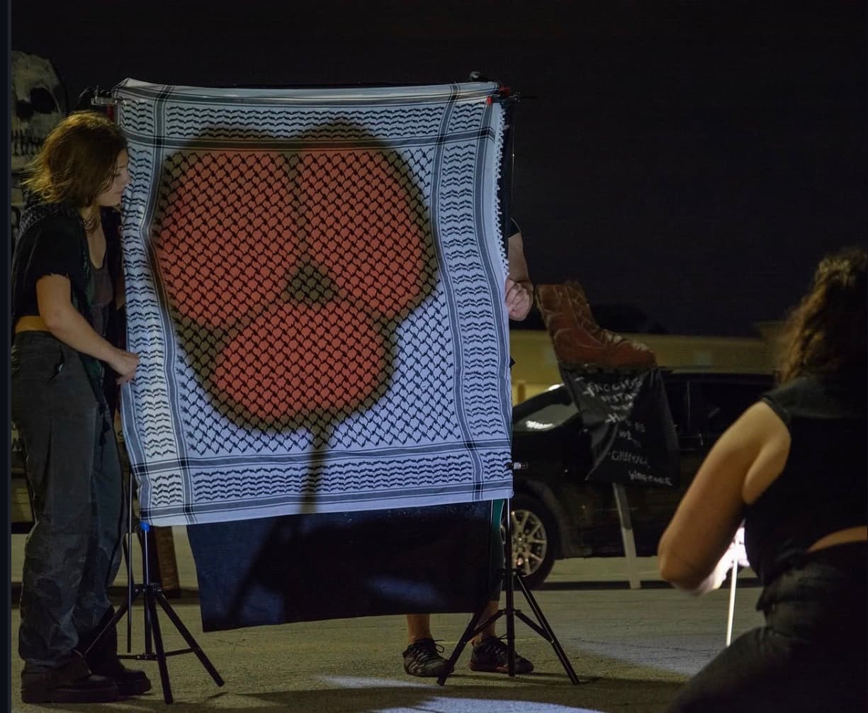 A red poppy silhouette projected onto a keffiyeh shadow-puppet screen at night