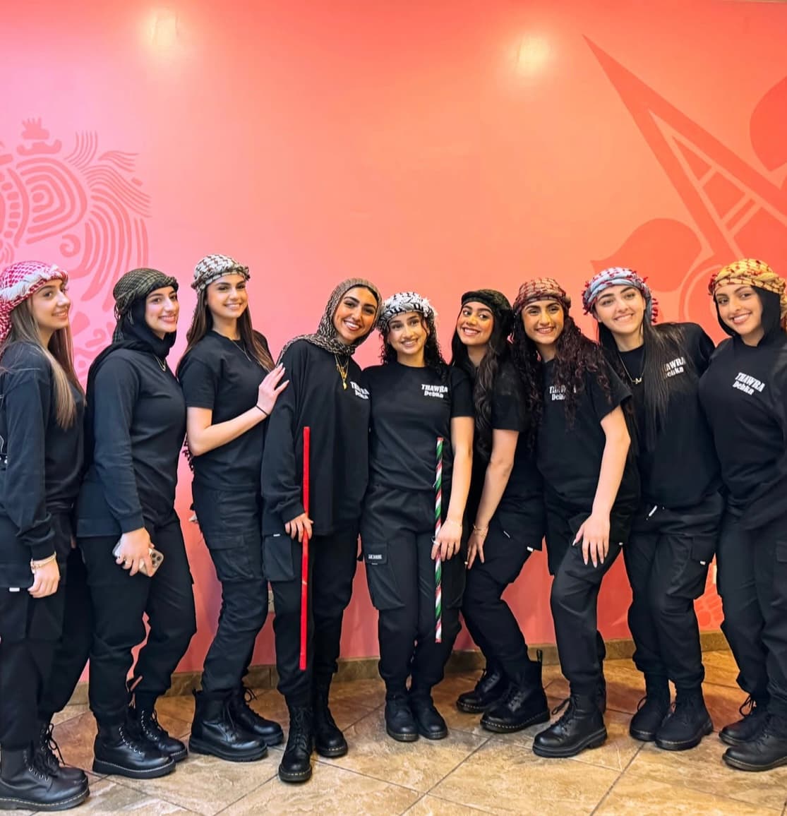 The Thawra Dabke troupe, nine performers in black with keffiyehs, holding dabke canes
